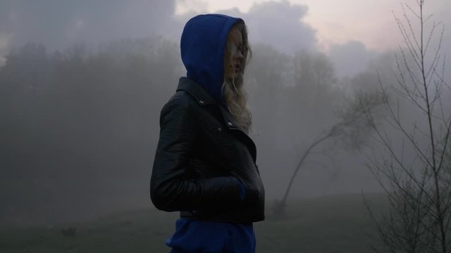 Close up shot of scared female whom suddenly turns after hearing strange sounds in foggy river bank. Dark view.