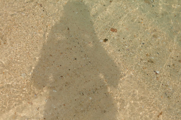 Shadow of a man on the sandy shore of a sea beach in the waves of water. Natural background.