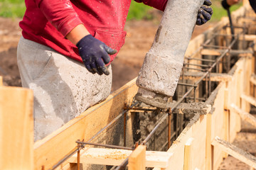 Close up of construction worker laying cement or concrete into the foundation formwork with automatic pump