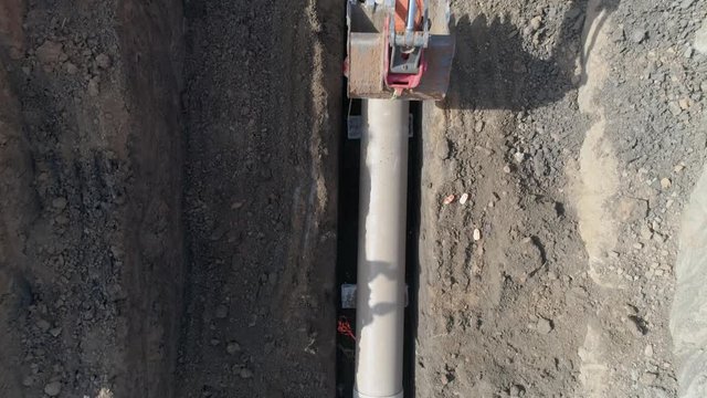 Concrete pipe tube installation. Aerial above men at work outside with heavy machinery to connect and install water or sewerage pipeline in a digging soil land