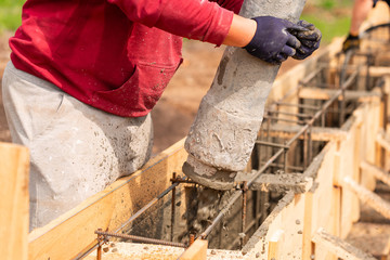 Close up of construction worker laying cement or concrete into the foundation formwork with automatic pump