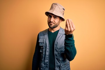 Handsome tourist man with beard on vacation wearing explorer hat over yellow background Doing Italian gesture with hand and fingers confident expression