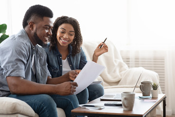 Young african american spouses checking documentation at home, reading insurance agreement