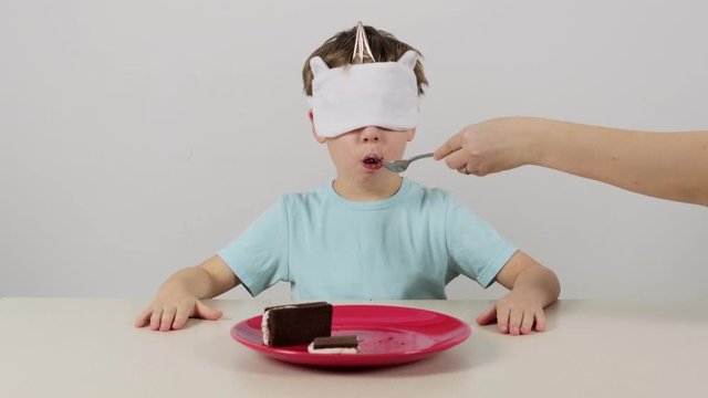 Little boy in a mask tries and guesses chocolate cake with white cream