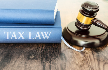 close-up of judge gavel and book with text TAX LAW on rustic wooden table