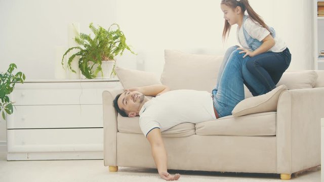 Father is tiered after playng with her little daughter on white sofa in 4k slowmotion video.