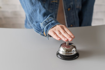 Hand of guest in a denim jacket ringing in silver bell. reception desk with copy space. Hotel service.