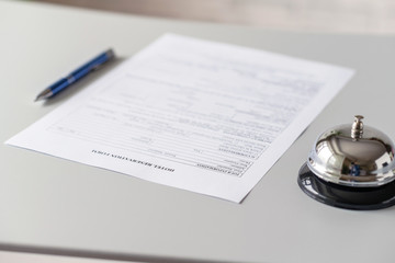Hotel reservation form and silver vintage bell on reception desk with copy space. Hotel service, registration. Selective focus