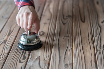 Hand of guest ringing silver vintage bell on wooden rustic reception desk with copy space. Hotel,...