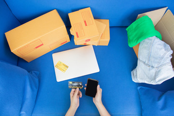 Fototapeta premium close up of the teenage shopper is laying on the sofa, and shopping online via smart phone with mock up credit card for digital technology world and seeing a lot of boxes beside her with the clothes.