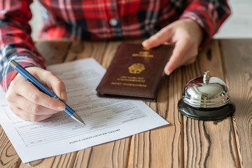Woman using Germany passport filling hotel reservation form in the hotel. Silver vintage bell on wooden rustic reception desk. Hotel service.