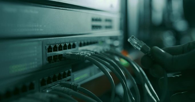 Datacenter technician attaches a new RJ45 ethernet cable to the networking switch in a rack full of equipment