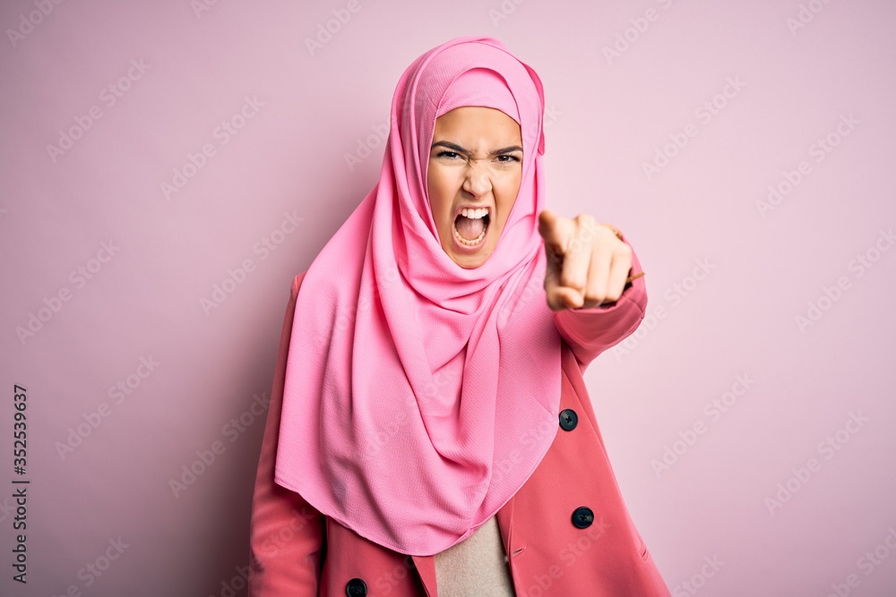 Sticker Young beautiful girl wearing muslim hijab standing over isolated pink background pointing displeased and frustrated to the camera, angry and furious with you