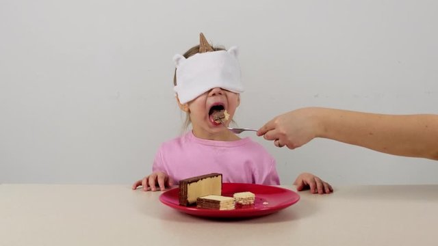 Little girl in a mask tries and guesses waffles with chocolate