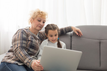 Side view of a grandmother and granddaughter using laptop in living room at home