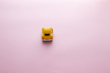 Minimal concept of a small yellow toy car on a beautiful surface, rear view