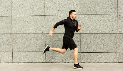 Sporty young guy running in city center with earphones