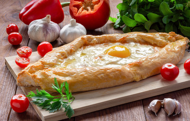 Khachapuri in Adjarian. Traditional Georgian cuisine. Open pie with Suluguni cheese and egg yolk in the shape of a boat on a wooden Board.