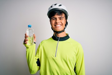 Young handsome cyclist man wearing security bike helmet drinking bottle of water with a happy face standing and smiling with a confident smile showing teeth