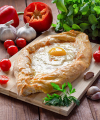 Khachapuri in Adjarian. Traditional Georgian cuisine. Open pie with Suluguni cheese and egg yolk in the shape of a boat on a wooden Board.
