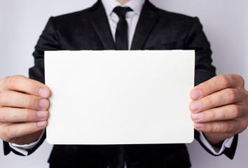 A young businessman holds in his hands an empty sheet of paper on a white background. A place for your advertising in business.