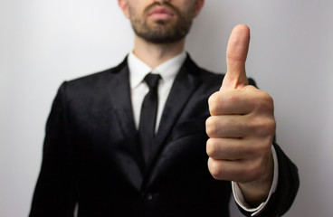 Young businessman with a beard shows a tin thumb up. Isolated on a white background in a jacket, white shirt and tie. Success concept.