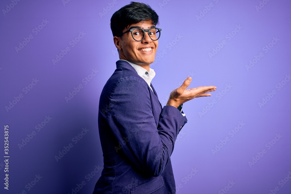 Wall mural Young handsome business man wearing jacket and glasses over isolated purple background pointing aside with hands open palms showing copy space, presenting advertisement smiling excited happy