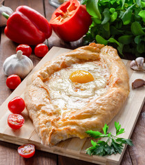 Khachapuri in Adjarian. Traditional Georgian cuisine. Open pie with Suluguni cheese and egg yolk in the shape of a boat on a wooden Board.