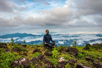 Fototapeta premium man meditating on rock isolated at the serene nature with amazing cloud layers in background
