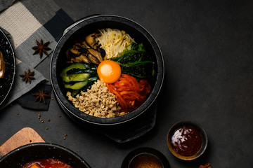 Korean Food Style : Top view of bibimbap or pibimpap in the black bowl. The main ingredients are yolk egg , Shiitake mushrooms, minced chicken, bean sprouts, cucumbers, carrots and pickles with rice
