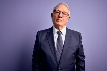 Grey haired senior business man wearing glasses and elegant suit and tie over purple background Relaxed with serious expression on face. Simple and natural looking at the camera.