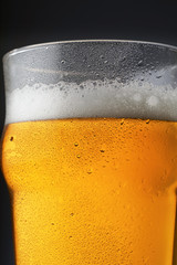 A pint of beer with foam in a glass with water drops on a dark background and reflection in the surface