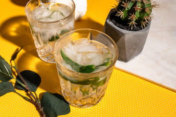 Fresh Mojito alcoholic cocktail with lime, rosemary, mint and ice in a crystal glass on yellow dots background.
