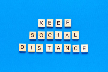Words keep social distance. Wooden inscription on a blue background. Information sign of keep social distance from blocks on a blue background.