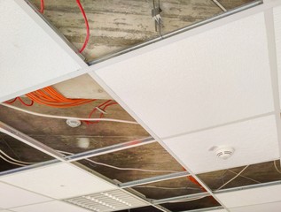 Partially open suspended ceiling, with plenum area and wires visible above acoustic panels and fixtures - obrazy, fototapety, plakaty