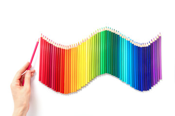 Rainbow wave of multicolored pencils isolated on white background. Female hand holds a wood red pencil. Back to school or drawing training concept.