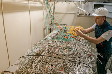 A technician connects a fiber optic internet cable in a server room. A worker in a helmet dissolves...