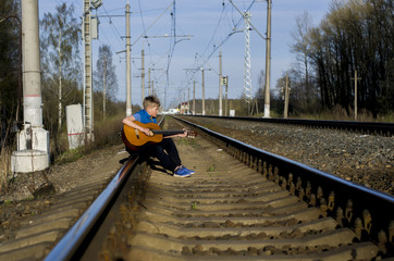 Naklejka premium a blonde teenage boy with a guitar on a railway, spring, adolescence and romance, first love, maturation and self-search, wandering in solitude, walking alone, loneliness