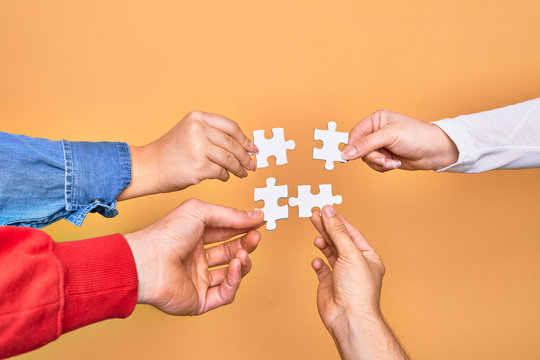 Hands of caucasian young people connecting pieces of puzzle over isolated yellow background