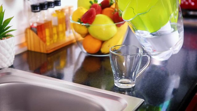 Pouring filtered water into glass from water filter jug in the kitchen. Purification and softening of drinking tap water. Closeup slow motion