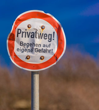 zerbeultes, besch&auml;digtes, Verkehrszeichen mit deutschem Text: Privatweg! Begehen auf eigene Gefahr
