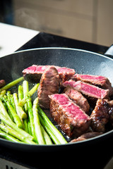Beef steak frying on the pan with baby asparagus