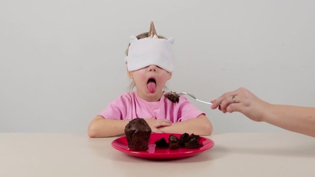 Little girl in a mask tries and guesses chocolate muffin
