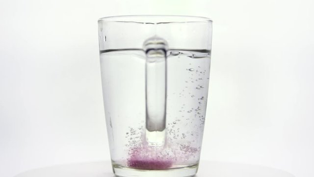 In a glass with water, a soluble, instant or dissolve pink tablet bubbles.