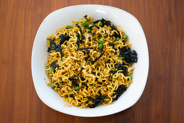 Vegetarian noodles - Fried noodles with composition: fried eggs, fried seaweed and peas on a wooden table