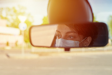 Woman in protective mask driving car, reflection in mirror
