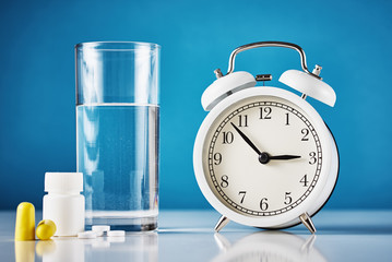 Insomnia problem and sleeping trouble concept. Alarm clock, glass of water, ear plugs and pills on...