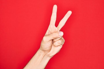 Hand of caucasian young man showing fingers over isolated red background counting number 2 showing two fingers, gesturing victory and winner symbol