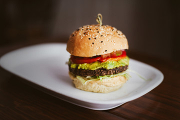 Fresh burger with meat, ketchup, avocado, guacamole on a white place on dark wooden table