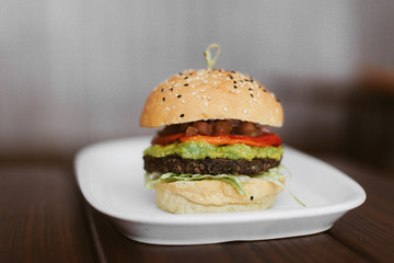 Fresh burger with meat, ketchup, avocado, guacamole on a white place on dark wooden table